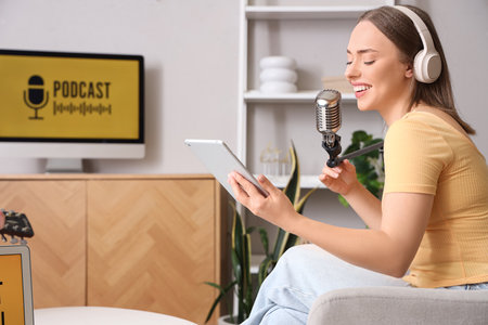 Young woman with tablet computer recording podcast in studioの写真素材