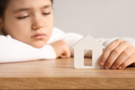 Sad girl with house figure at table in room, closeup. Adoption conceptの写真素材