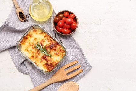 Baking dish with tasty pasta, rosemary, peppercorns, tomatoes and jug of oil on light backgroundの写真素材