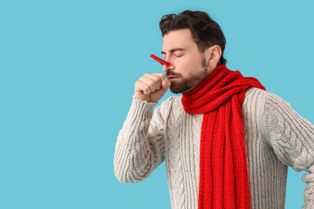 Young man with a red object in his nose against blue background. Stuffy nose conceptの写真素材