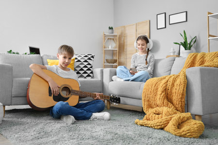Teenage boy playing guitar and his sister in headphones using mobile phone at homeの写真素材