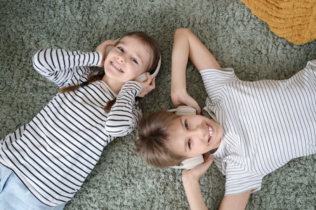 Teenage boy with his sister in headphones lying on carpet, top viewの写真素材