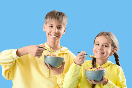 Teenage boy with his sister eating cereal rings on blue backgroundの写真素材