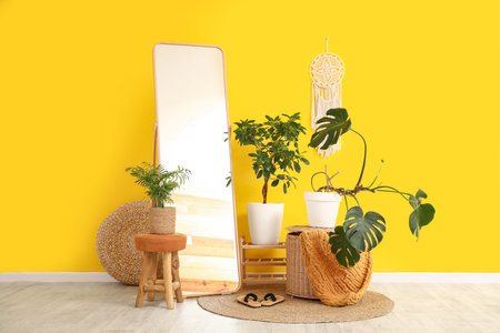 Pouf, floor mirror and houseplants near yellow wall in interior of roomの写真素材