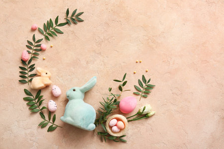 Frame made of Easter eggs, decorative nest, rabbits and green leaves on beige grunge background