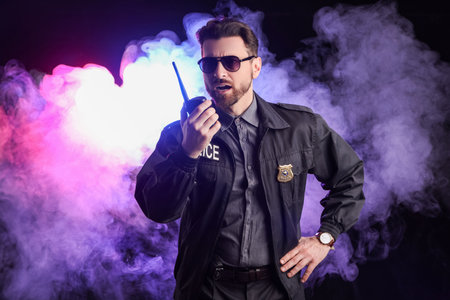 Male police officer with radio transmitter in smoke on black backgroundの写真素材