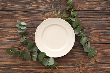 Stylish table setting with plate and eucalyptus branches on wooden background