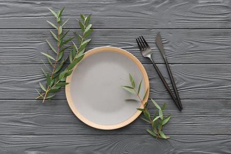 Stylish table setting with plate, cutlery and plant branches on gray wooden backgroundの写真素材