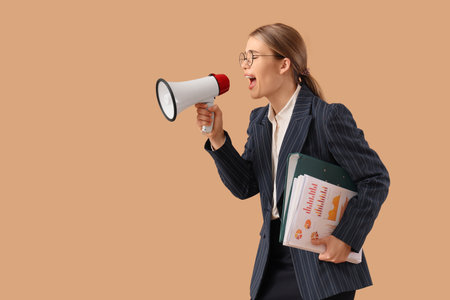 Young businesswoman with papers shouting into megaphone on beige backgroundの写真素材