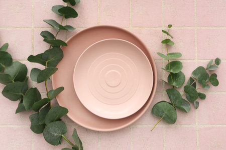 Stylish table setting with plates and eucalyptus branches on pink tile background