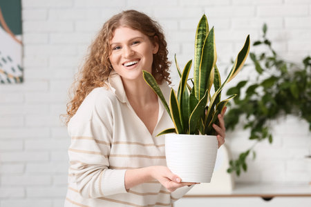 Pretty young woman with sansevieria plant at homeの写真素材