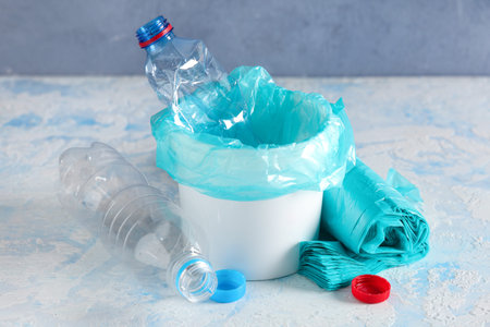 Bucket with garbage bags, plastic bottles and caps on color background