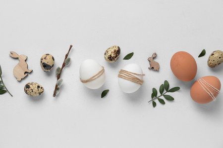 Composition with wooden rabbits, Easter eggs, green leaves and pussy willow branch on white...