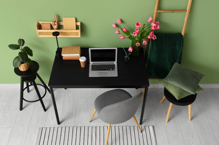 Stylish workspace with modern laptop, books and bouquet of beautiful tulip flowers near green wallの写真素材