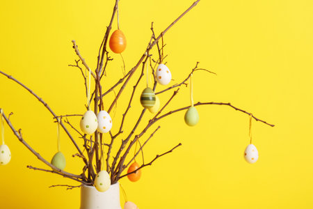Vase with tree branches and colorful Easter eggs on yellow backgroundの写真素材