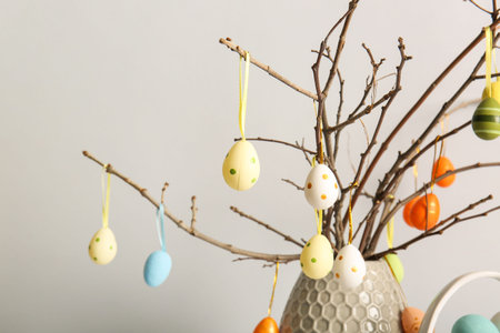 Vase with tree branches and colorful Easter eggs on white background