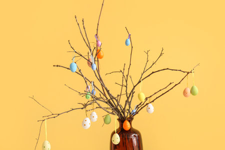 Vase with tree branches and colorful Easter eggs on yellow backgroundの写真素材