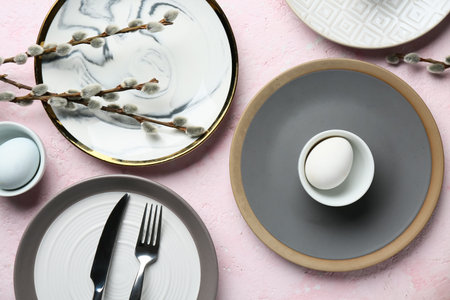 Different clean plates with Easter eggs and pussy willow branches on light pink background