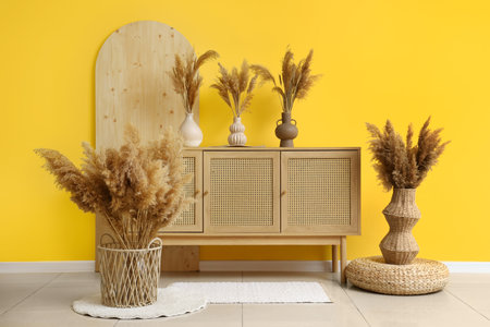Chest of drawers and pampas grass in vases near yellow wall in roomの写真素材