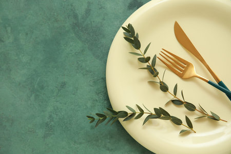 Beautiful table setting with golden cutlery and eucalyptus branches on green background, closeup