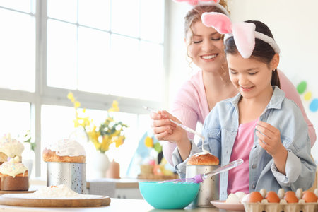 Happy mother and her daughter glazing Easter cake in kitchen