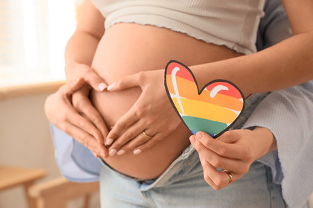 Young pregnant lesbian couple with LGBT heart at home, closeup