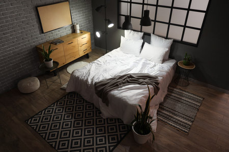 Interior of modern bedroom with cozy bed and glowing lamps at nightの写真素材