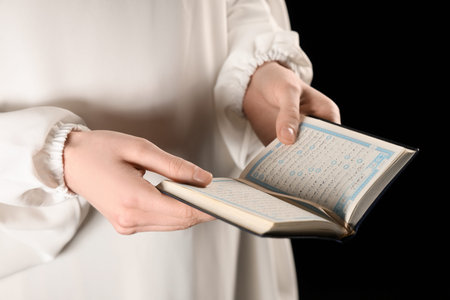 Muslim woman with Koran on black background, closeup. Ramadan celebration