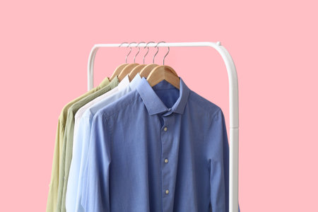 Rack with stylish collar shirts on pink background