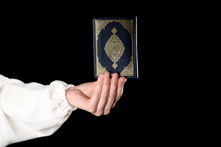 Hand of Muslim woman with Koran on black background. Ramadan celebrationの写真素材