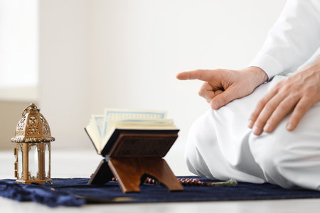 Muslim man with Koran and fanoos praying on prayer carpet at home. Ramadan celebrationの写真素材