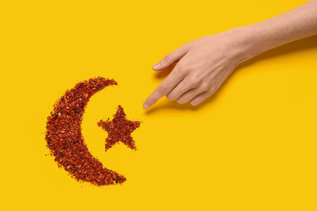 Female hand with crescent and star made of chili flakes on yellow background, closeup. Ramadan celebrationの写真素材