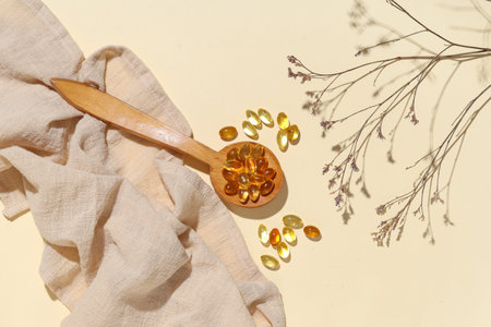 Composition with wooden spoon of fish oil capsules, napkin and dried flowers on color backgroundの写真素材