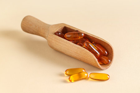 Wooden scoop with fish oil capsules on color backgroundの写真素材