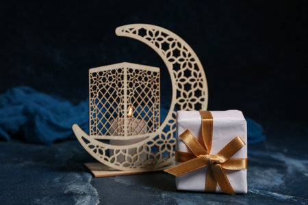 Crescent with burning candle and gift box on blue grunge background. Ramadan celebration