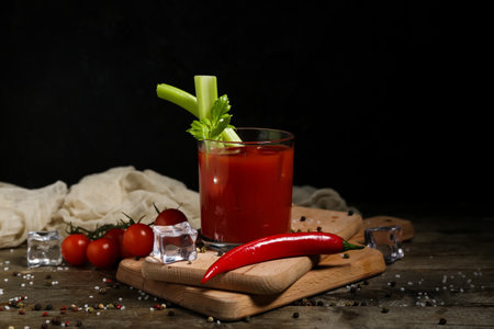 Glass of bloody mary cocktail with celery, chili pepper and peppercorns on wooden tableの写真素材