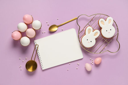 Composition with blank notebook for recipes, Easter eggs and cookies on lilac background