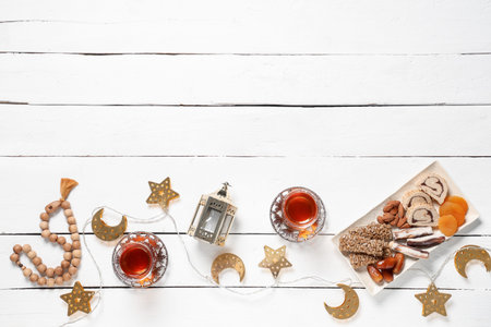 Glasses of tasty Turkish tea with sweets, fanoos and tasbih on white wooden background. Ramadan...