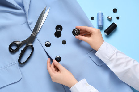 Female hands with black buttons, scissors, threads and jacket on blue backgroundの写真素材
