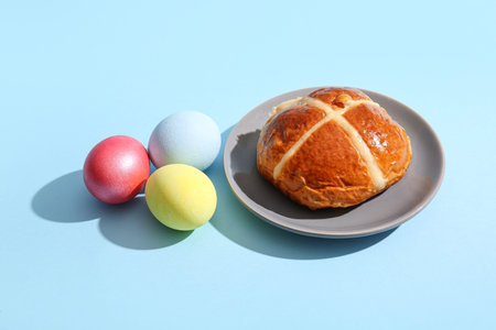 Plate with Easter bun and eggs on blue background