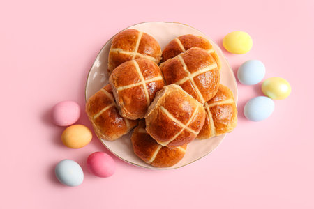 Plate with Easter cross buns and eggs on pink background