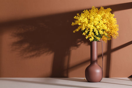 Vase with mimosa flowers on white table against brown backgroundの写真素材