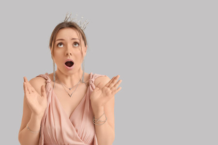 Surprised young woman in prom dress with tiara on gray backgroundの写真素材