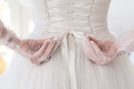 Beautiful bride tying corset in bedroom, back viewの写真素材