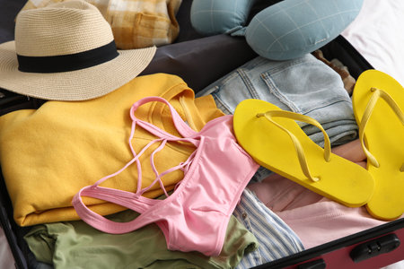 Unpacked suitcase with clothes and flip-flops on bed in hotel room, closeupの写真素材