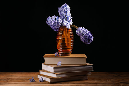 Vase with bouquet of beautiful purple hyacinth flowers and books on wooden table near black wallの写真素材