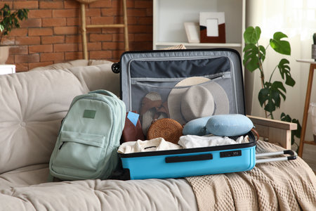 Unpacked suitcase with clothes and travel accessories on sofa in living roomの写真素材
