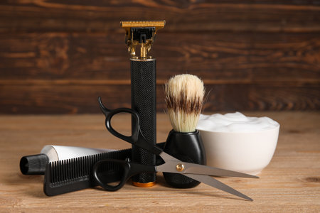 Modern trimmer with scissors, shaving brush and bowl of cream on wooden backgroundの写真素材