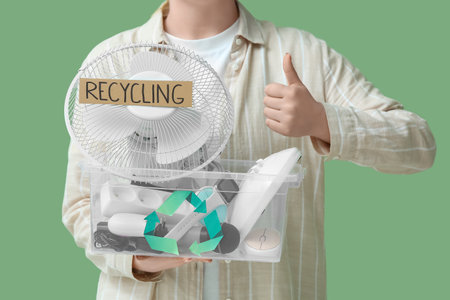 Woman with electronic waste for recycling in container showing thumb-up on green backgroundの写真素材