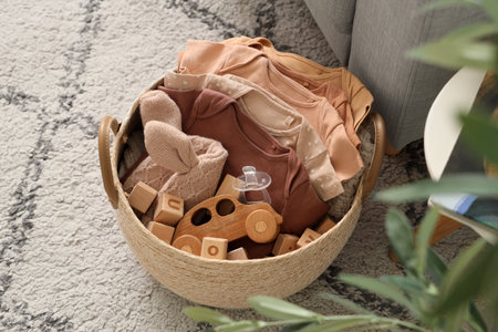 Basket with baby clothes and toys on carpet in roomの写真素材